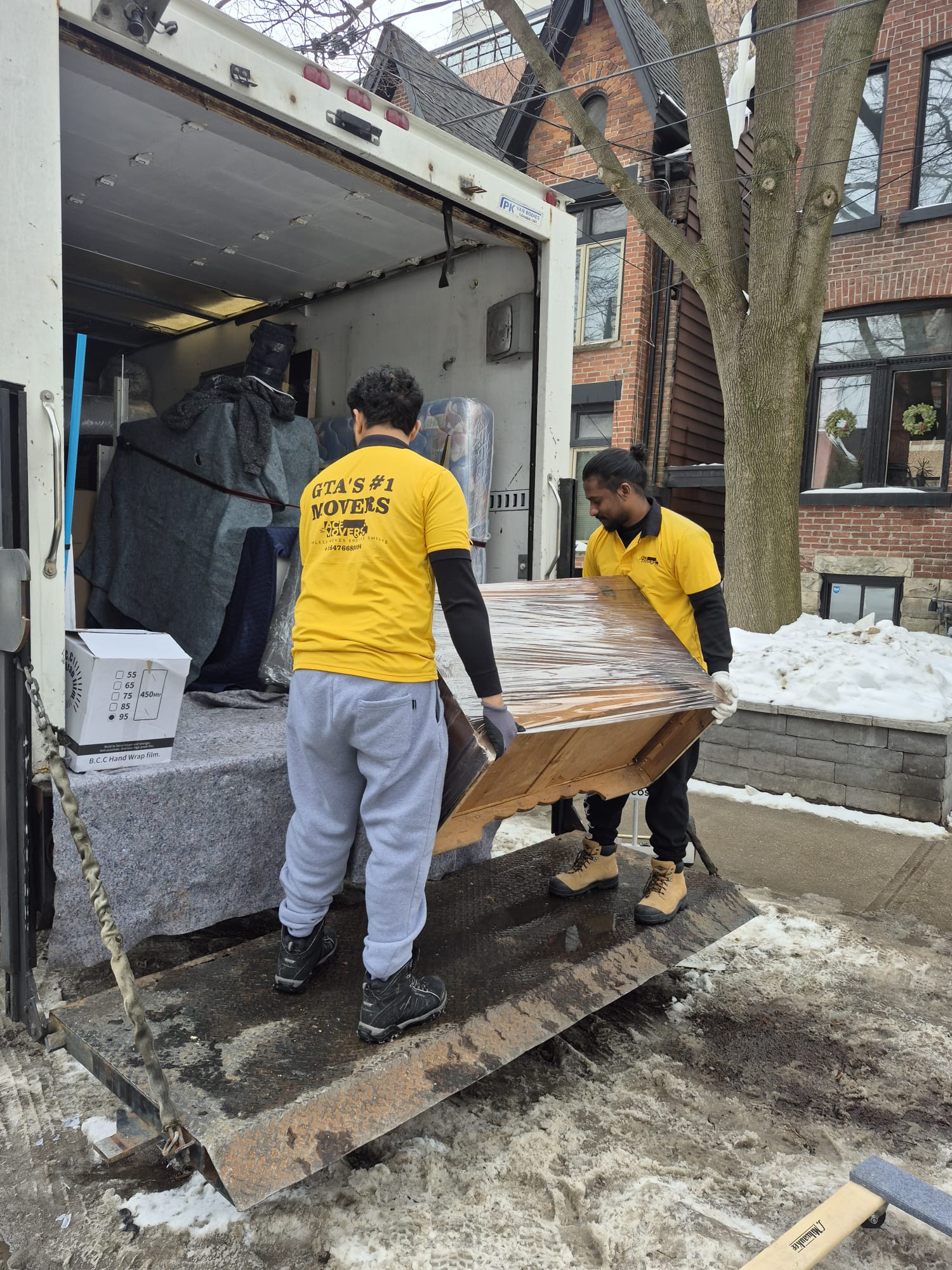 Two Acemovers crew members loading wrapped furniture into a moving truck in winter